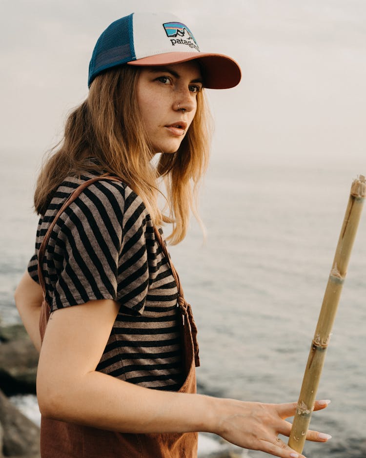 Female In Cap With Bamboo Stick Near Sea