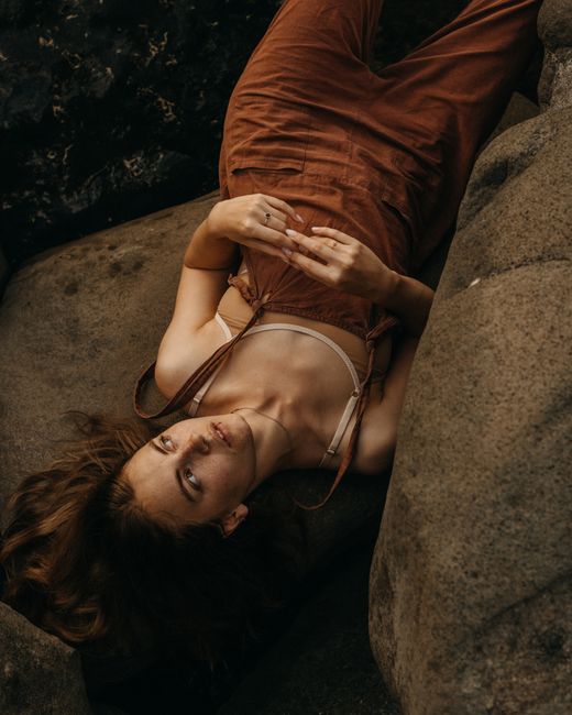 Top view of pensive female with bare shoulders looking away and connecting flingers while lying on stone