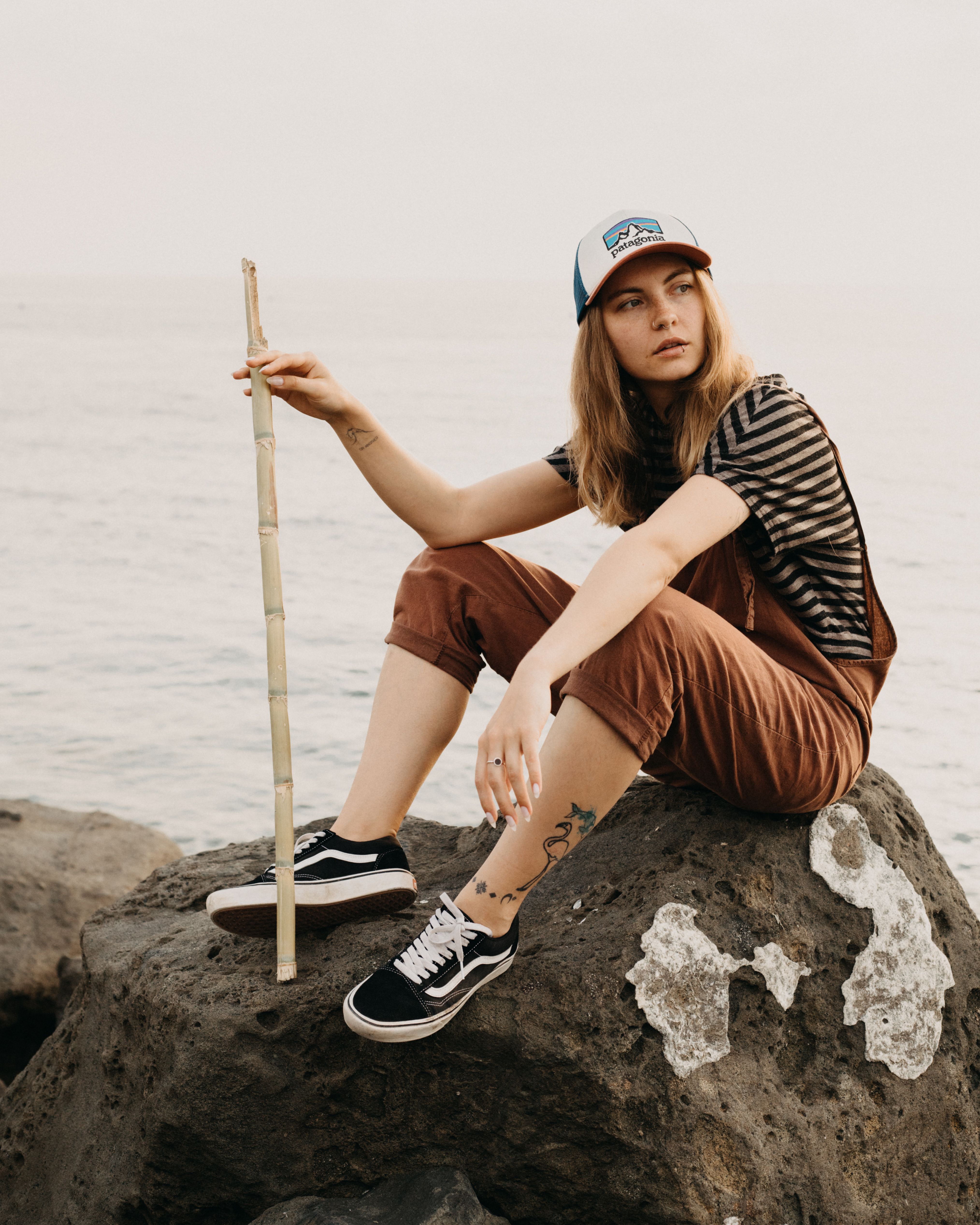 Stylish woman sitting on stone near sea · Free Stock Photo
