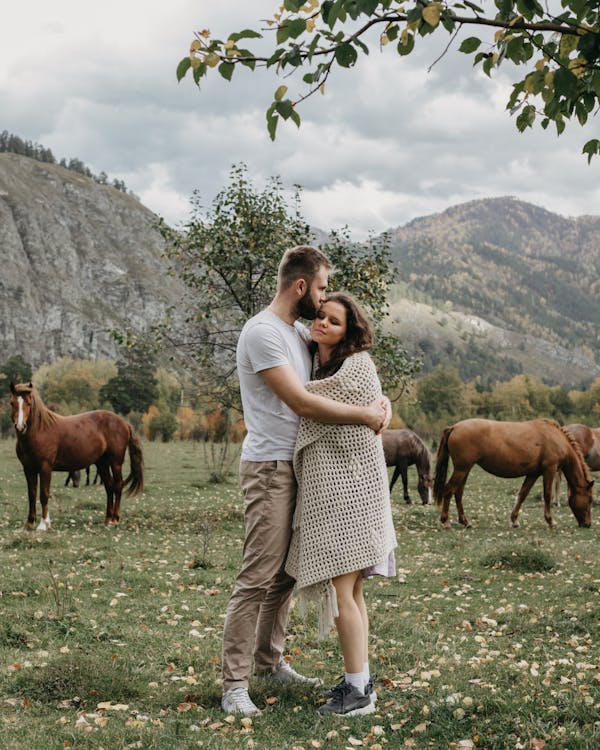 Free Romantic couple hugging on grassy meadow near mountains Stock Photo