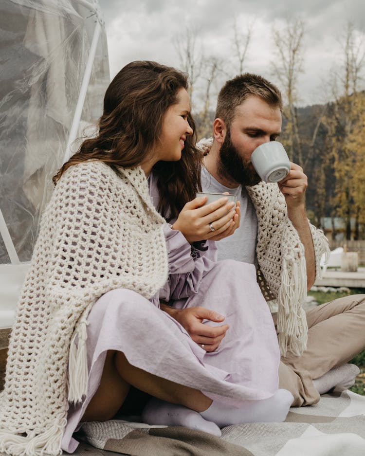 Couple With Hot Drink Wrapped In Knitted Shawl