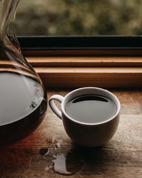 Free Mug with coffee near glass vessel on windowsill Stock Photo