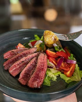 Delicious beef steak salad with vegetables served on a dark plate, perfect for gourmet lovers.