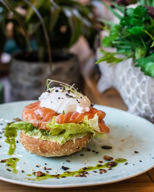 Free Tasty appetizing bun with salad and salmon served on white plate with poached egg on wooden table Stock Photo