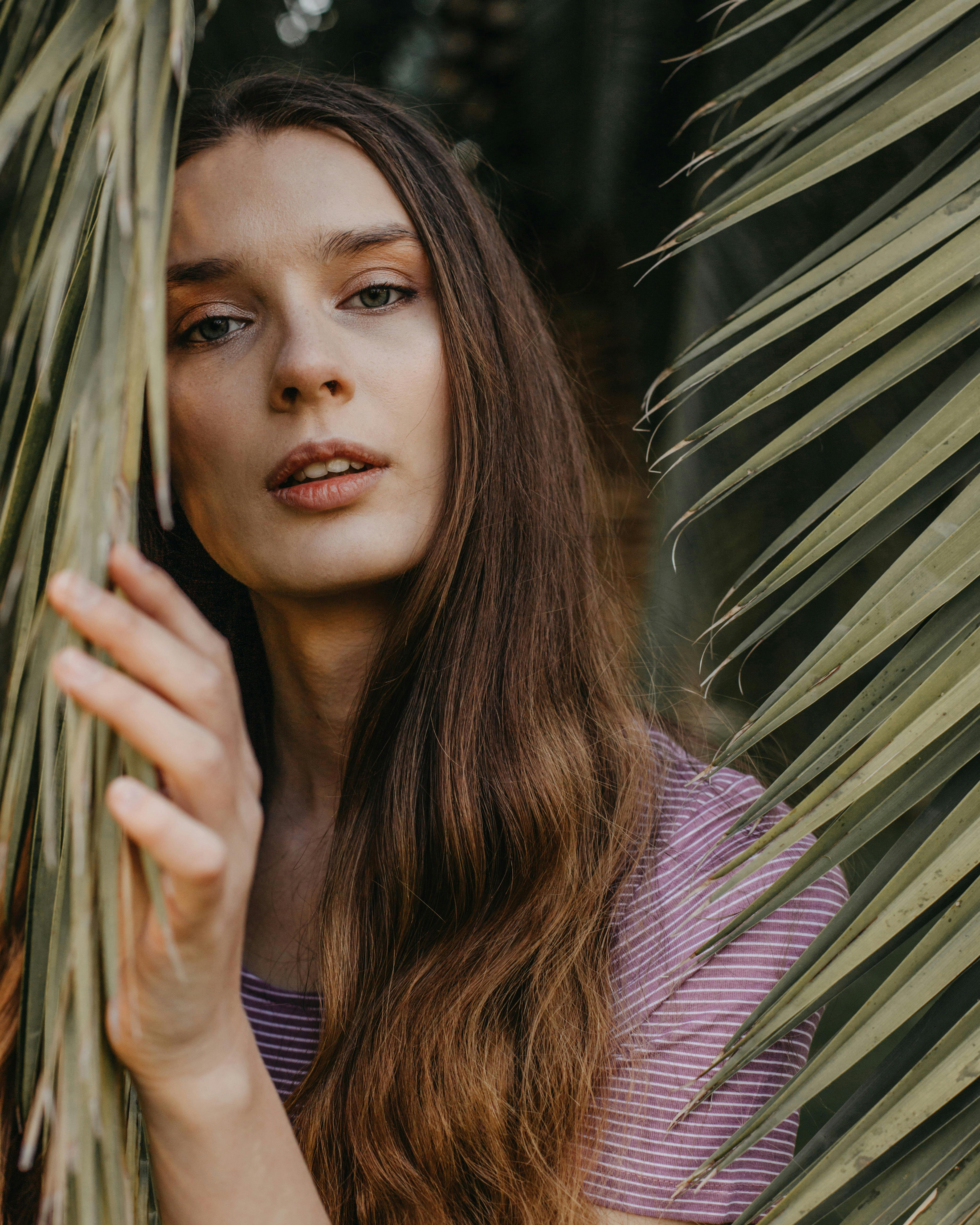 Young beautiful female with long hair looking at camera while standing near green exotic plants
