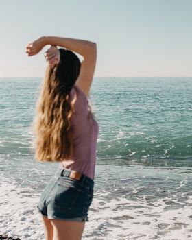 Back view of unrecognizable female in denim shorts standing on beach and enjoying summer holidays