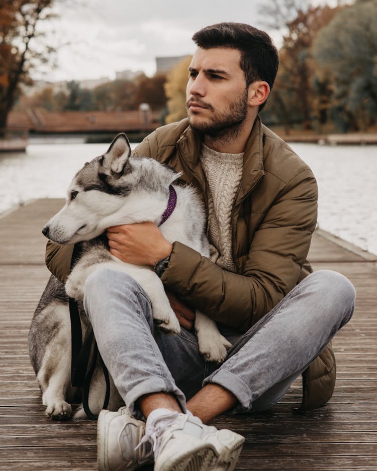 Person Sitting On Wooden Dock While Holding A Dog