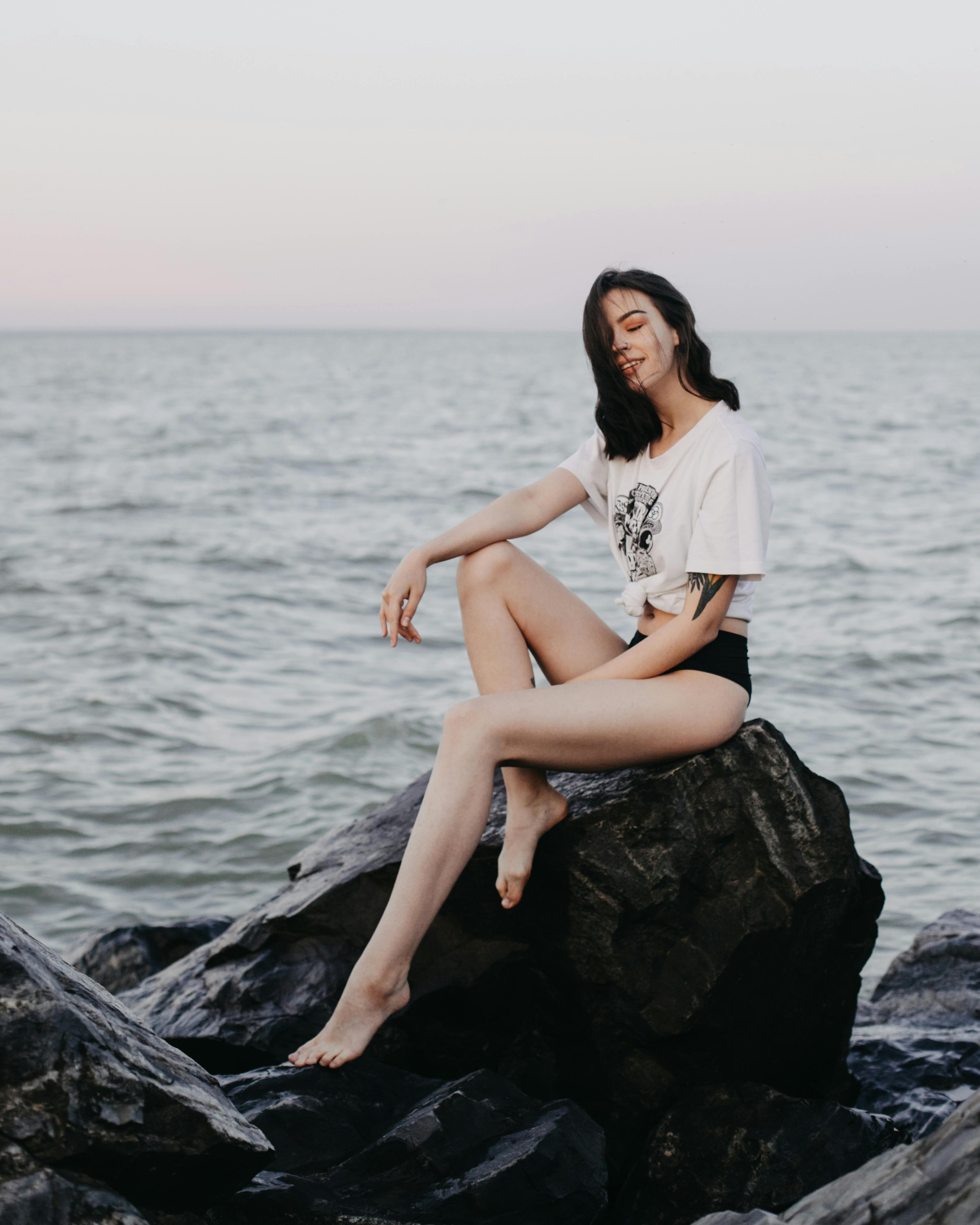 A woman poses gracefully on rocks by the sea, capturing a serene and tranquil moment.