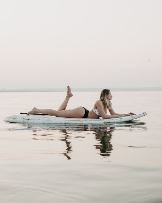 A woman lying on a paddleboard in calm waters at sunset, enjoying a peaceful moment.