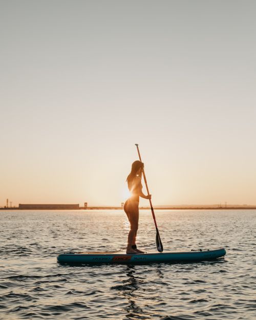 Free Silhouetted woman stand-up paddleboarding during a beautiful sunset. Tranquil outdoor scene. Stock Photo