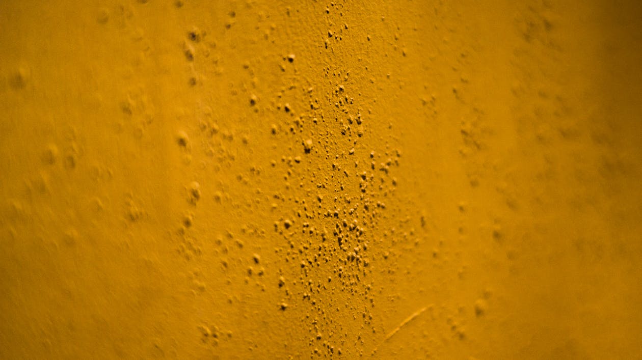 Background of uneven wall surface of yellow color with irregular grains in selective focus