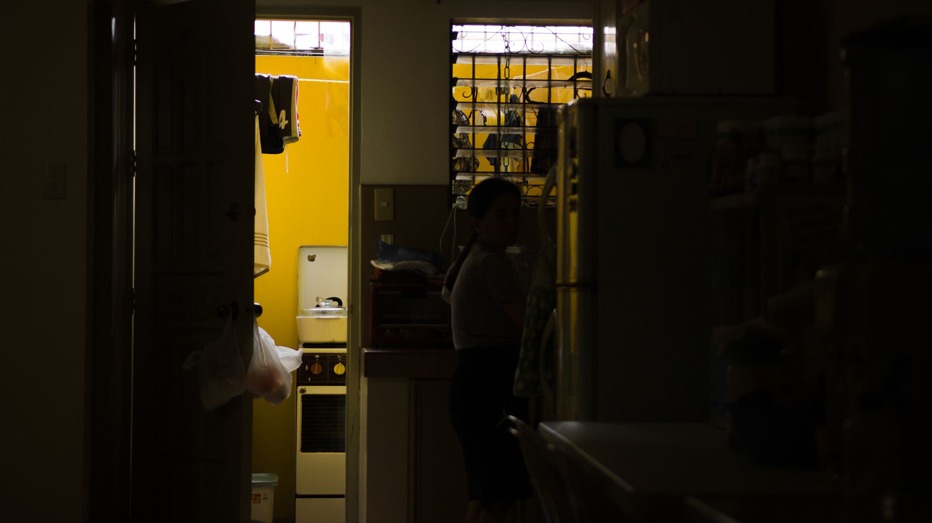Dark apartment with door ajar into small laundry room of yellow color with glowing lamps