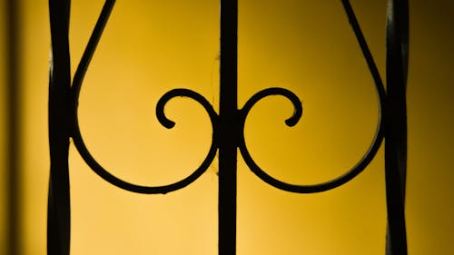 Metal fence with ornamental details against yellow wall