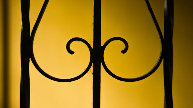 Close-up of ornate metal fencing with a vibrant yellow background, showcasing intricate details.