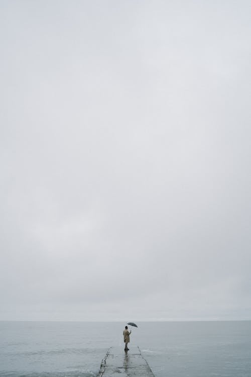 A Person Holding an Umbrella while Standing on a Concrete Pier