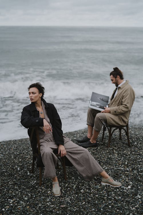 Free Man and Woman Sitting on Brown Wooden Chair on Gray Rocky Shore Stock Photo