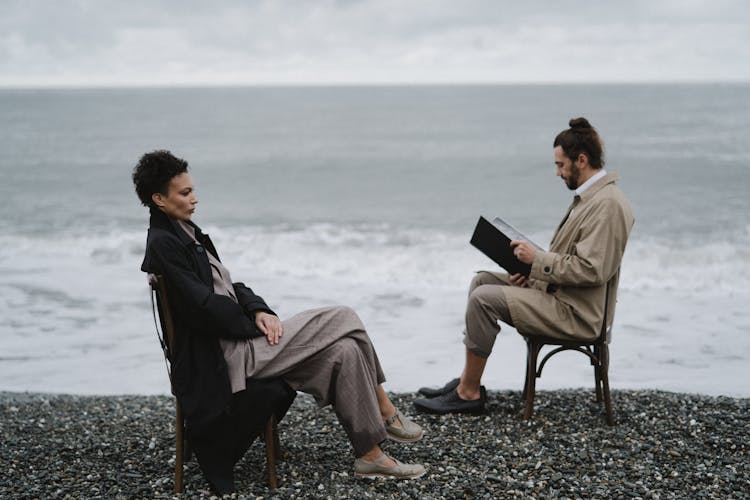 Man And Woman Sitting On Wooden Chair Near Beach