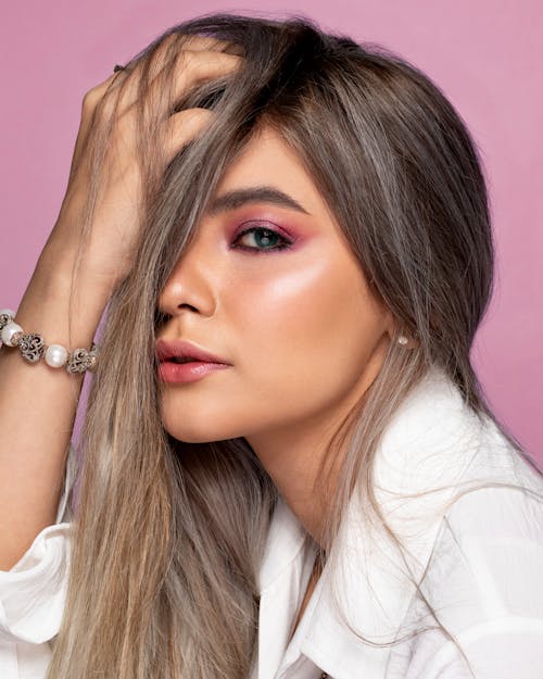 Side view of young woman with makeup covering half of face with long hair while looking at camera