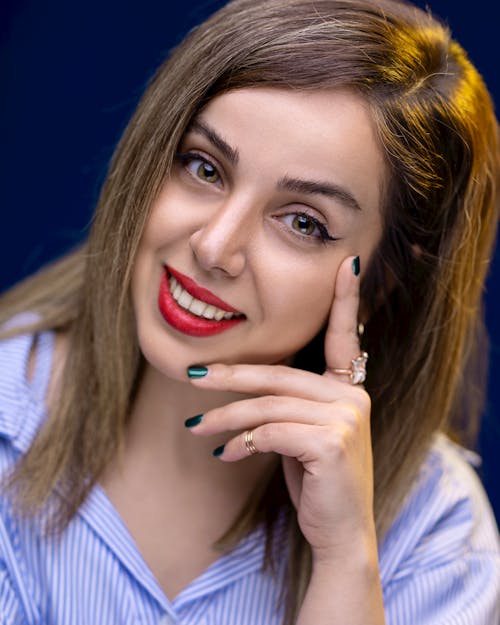 Alluring woman with makeup and brown hair touching face while looking at camera on dark background