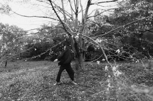 Grayscale Photo of Woman in Black Jacket and Pants dancing Near Bare Trees