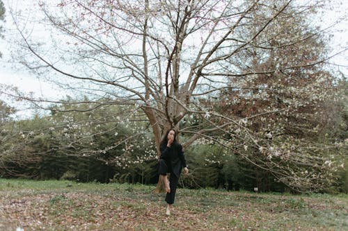 Woman in Black Clothes dancing near Bare Trees