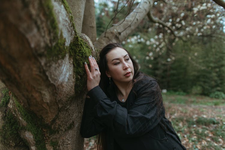 A Woman Leaning Her Head Against Mossy Tree Trunk