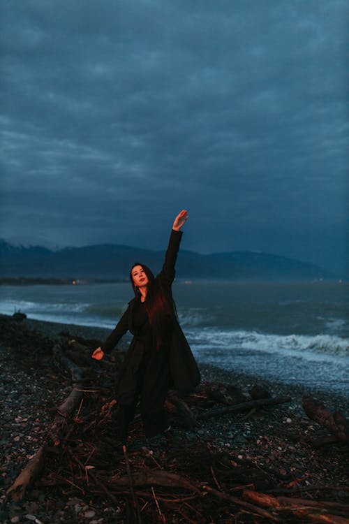 Woman in Black Coat and Pants dancing on Rocky Shore