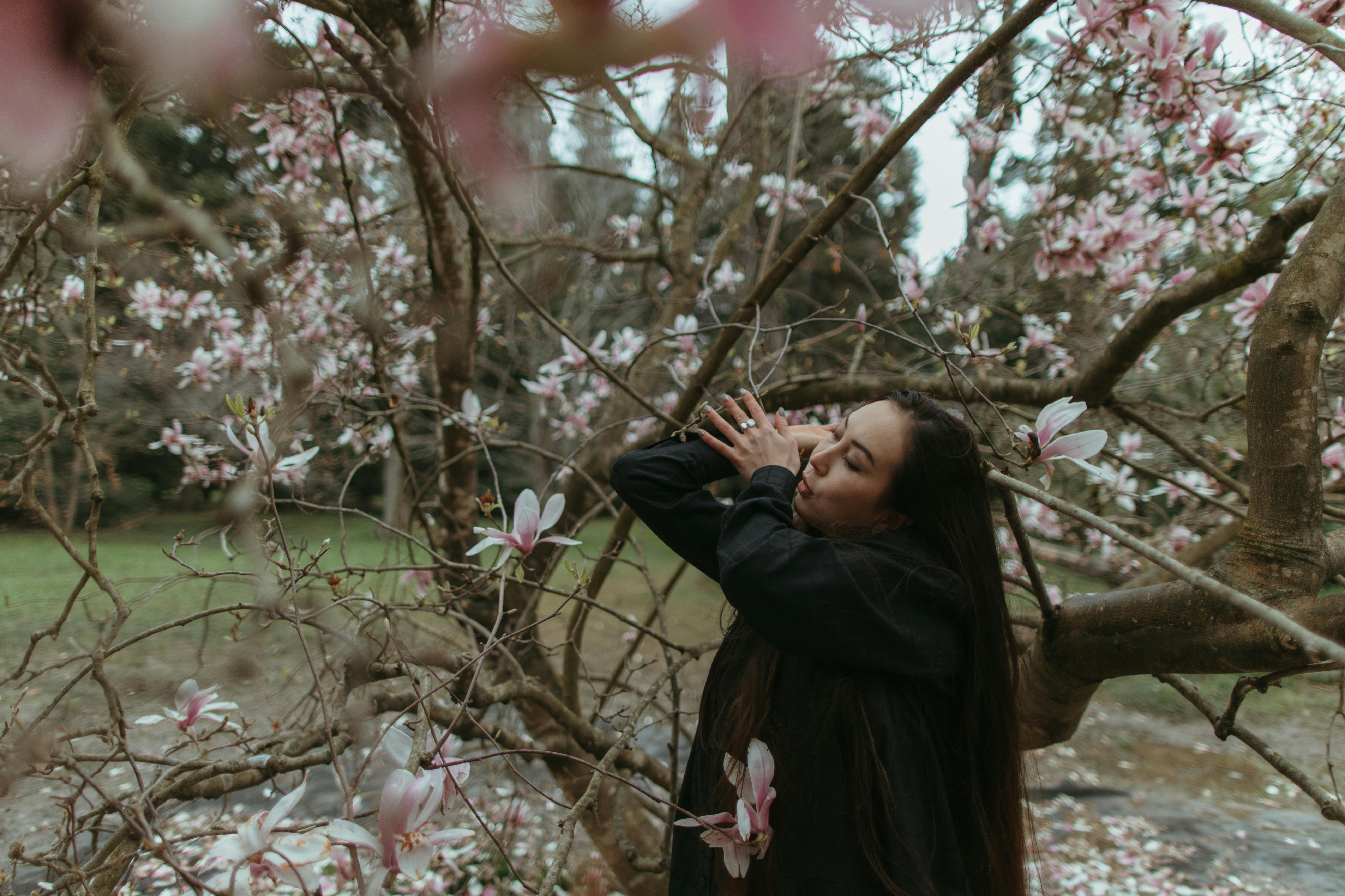 woman in black jacket standing under pink cherry blossom tree