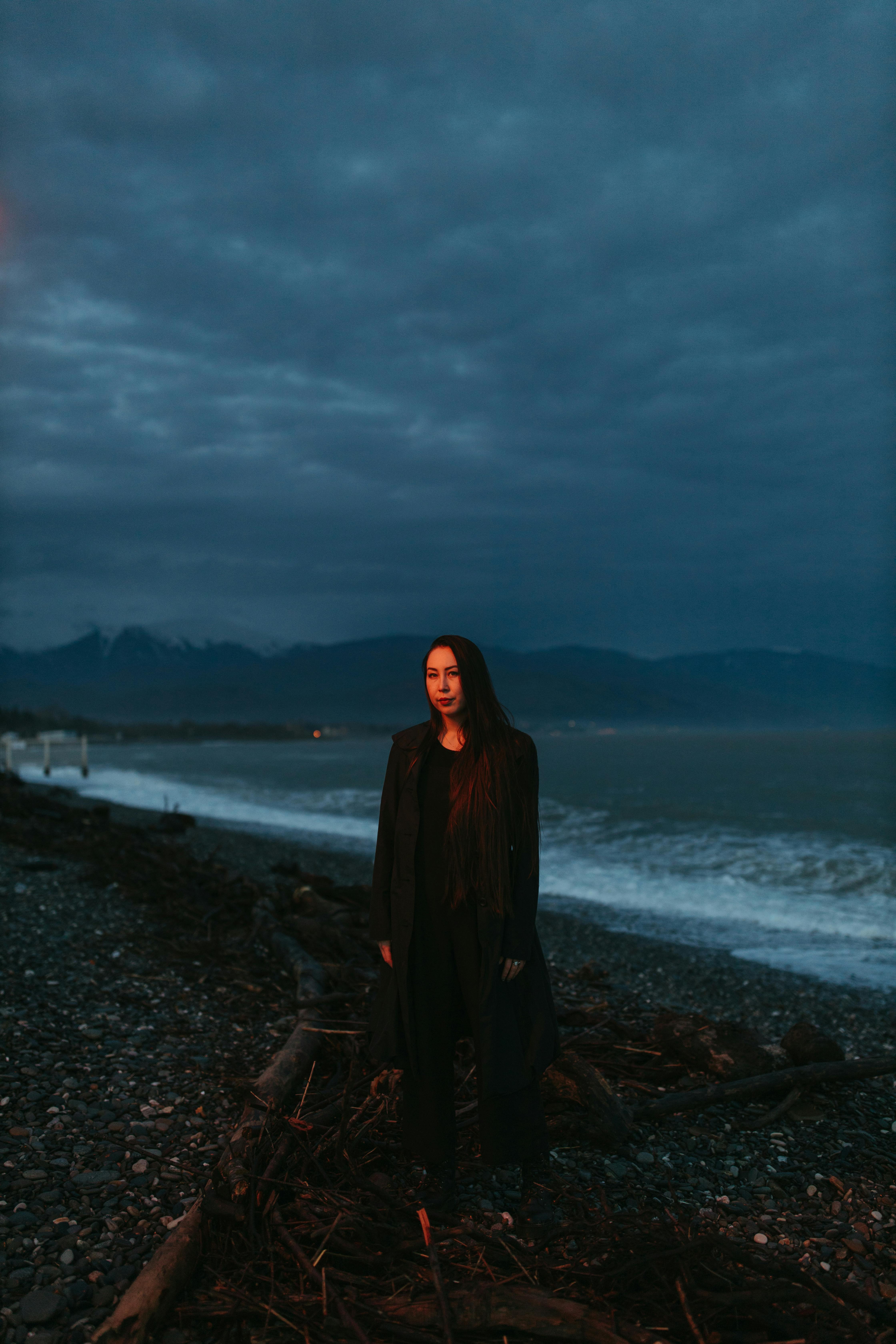 一个神秘的女人在黄昏时分站在海边的岩石海岸线上，捕捉到喜怒无常的沿海气氛