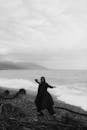 A Woman in Black Clothes Dancing on Rocky Shore