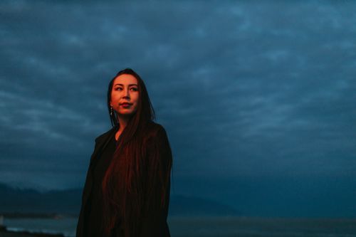Free A contemplative woman with long hair stands under a moody, blue evening sky, exuding elegance and mystery. Stock Photo