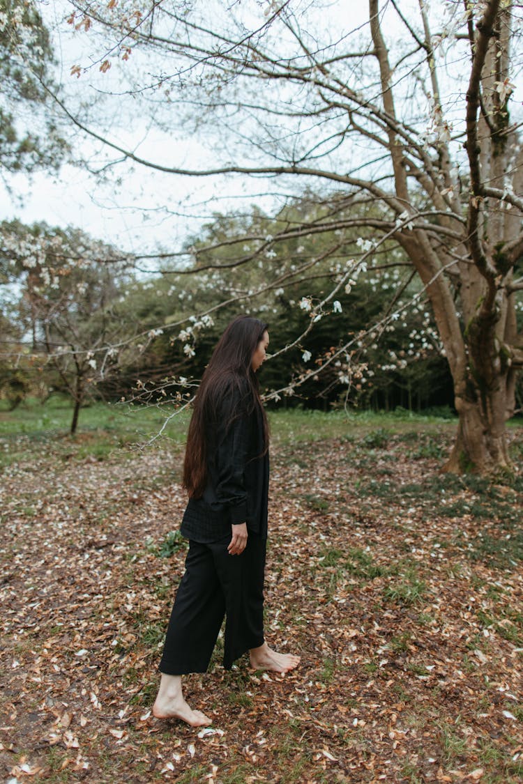 A Barefooted Person Walking On Ground Full Of Brown Dried Leaves