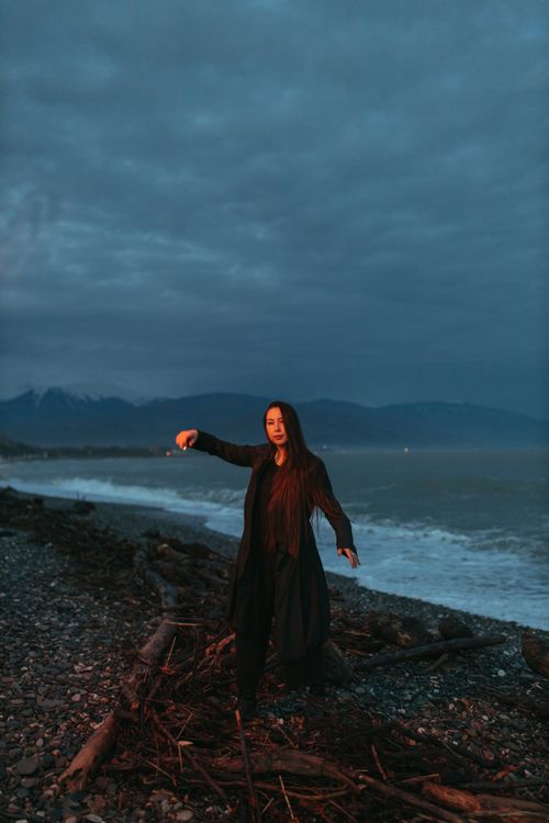 Free A woman stands gracefully on a rocky beach at twilight, with mountains in the background. Stock Photo