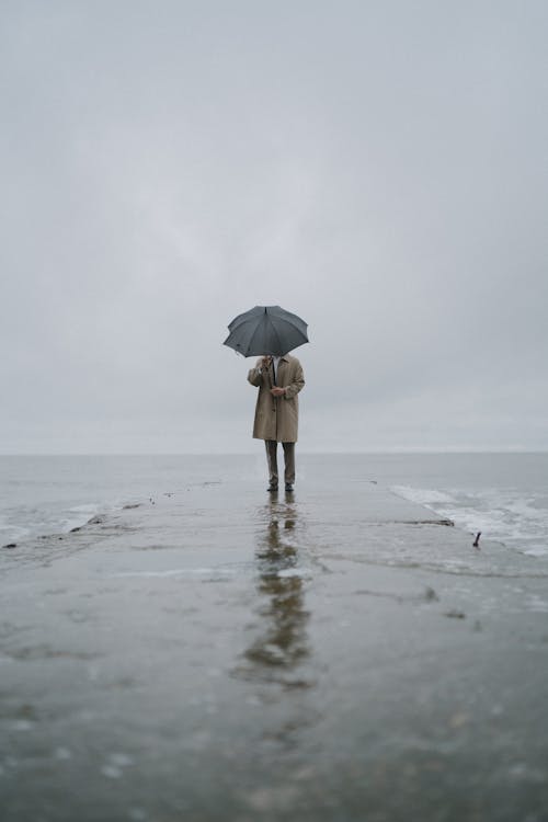 A Man Standing on Sea Dock Holding Umbrella 