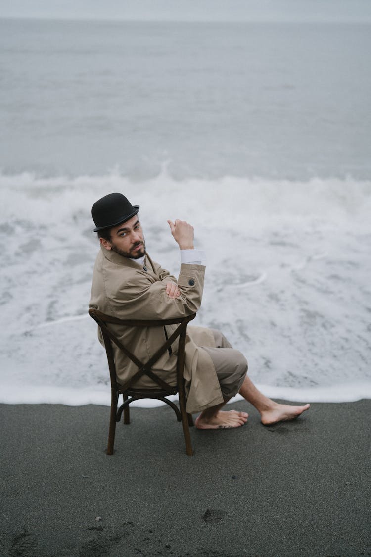 A Man In Brown Coat Sitting On Chair On The Beach