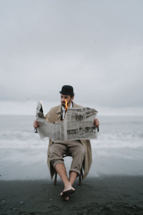 A Man Reading a Burning Newspaper on a Beach