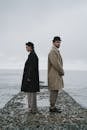 一对夫妇背靠背站在海边的一个多岩石的码头上，唤起隔离和沉思的主题