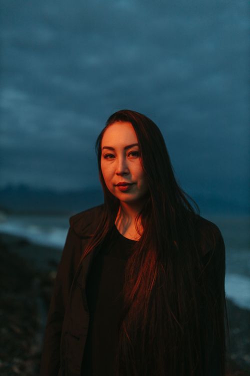 Free A serene portrait of a woman standing by the ocean at twilight, under a moody sky. Stock Photo