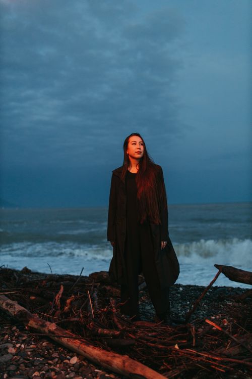 Free A woman in black clothing stands by the sea at twilight, exuding a moody and dramatic atmosphere. Stock Photo