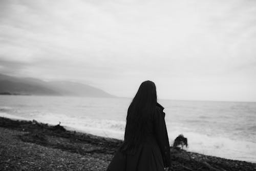 Grayscale of a Woman Woman Wearing Black Clothes on the Sea Shore
