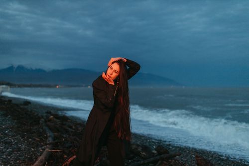 Free A woman in black clothing poses dramatically on a stormy seashore during twilight. Stock Photo