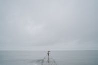 一个带伞的孤独的人站在码头上，在灰色多云的天空下延伸到广阔的大海上