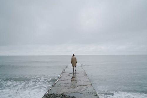 Back View of a Person Walking on Concrete Pier
