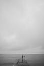 一个孤独的身影站在码头上，撑着一把雨伞，靠着阴暗的单色海景
