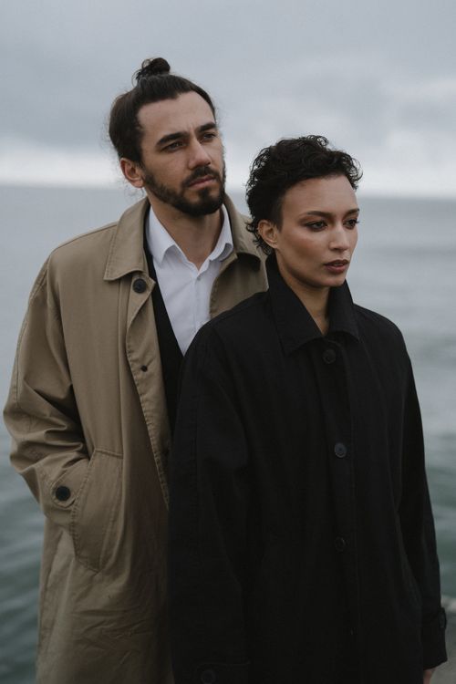 Free A stylish couple in coats stand by the sea, exuding fashion and elegance. Stock Photo