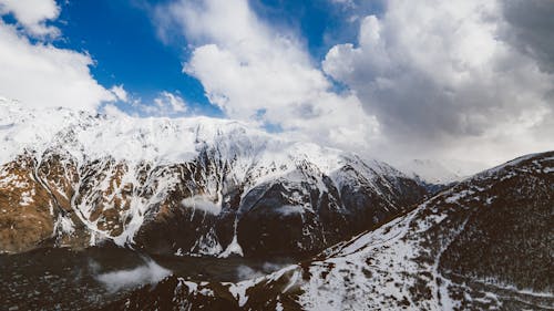 Snow Covered Rocky Mountains under Cloudy Sky 