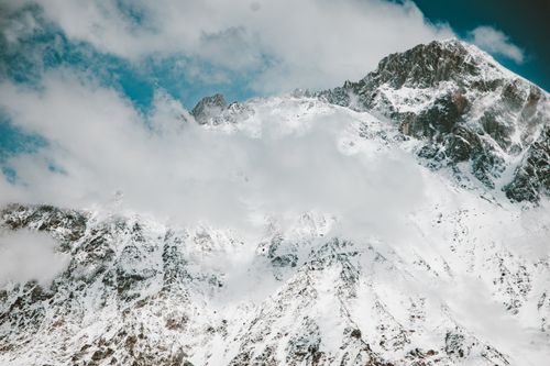 Free Snowy mountain peaks rise through the clouds, capturing winter's serene beauty. Stock Photo