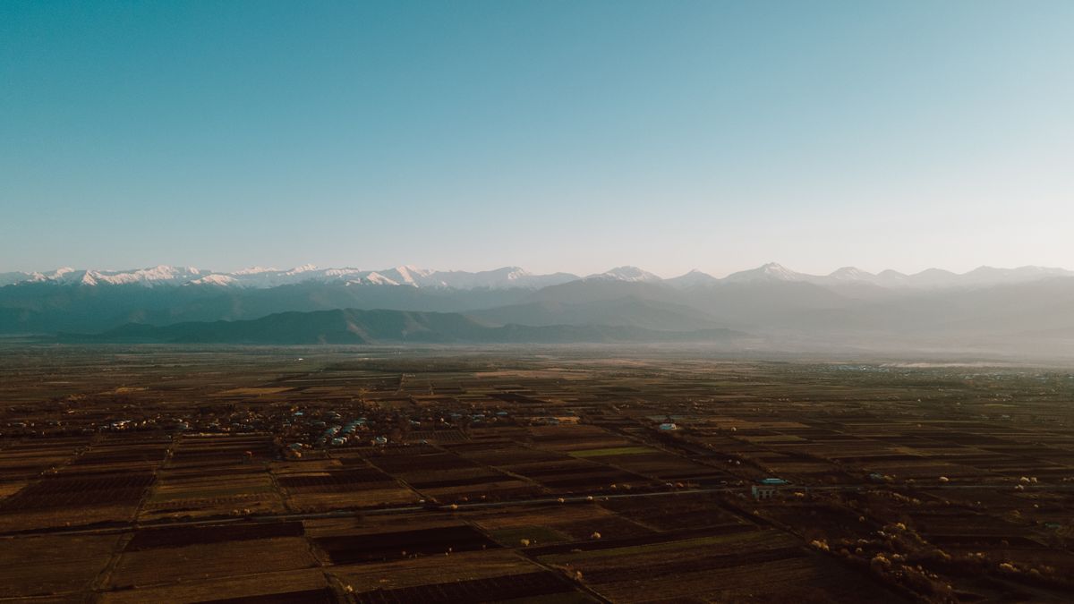 Breathtaking aerial view of expansive farmland with mountains in the distance under a clear blue sky.