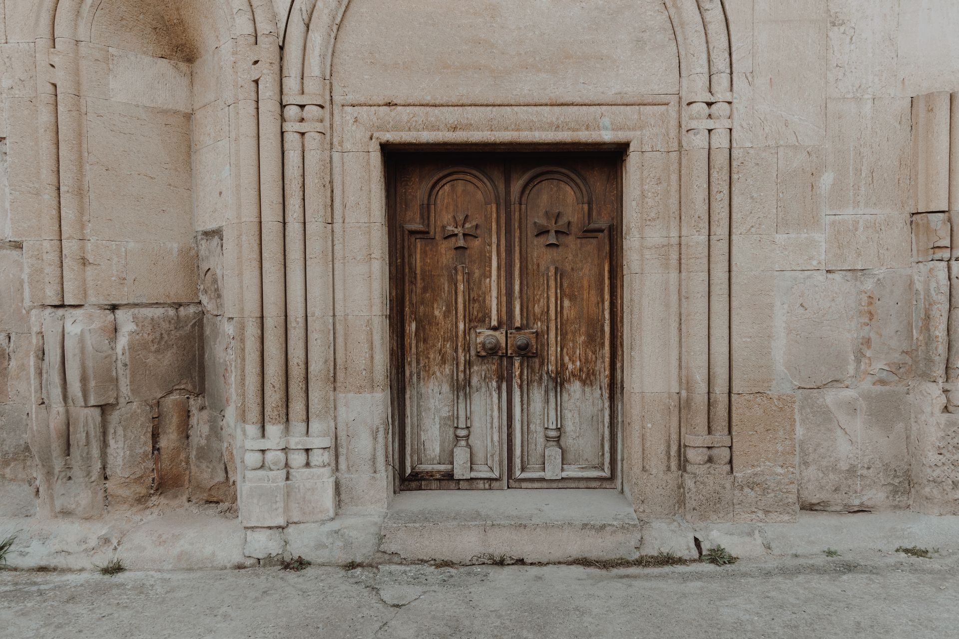 A historic wooden door with cross motifs on an ancient stone building facade.