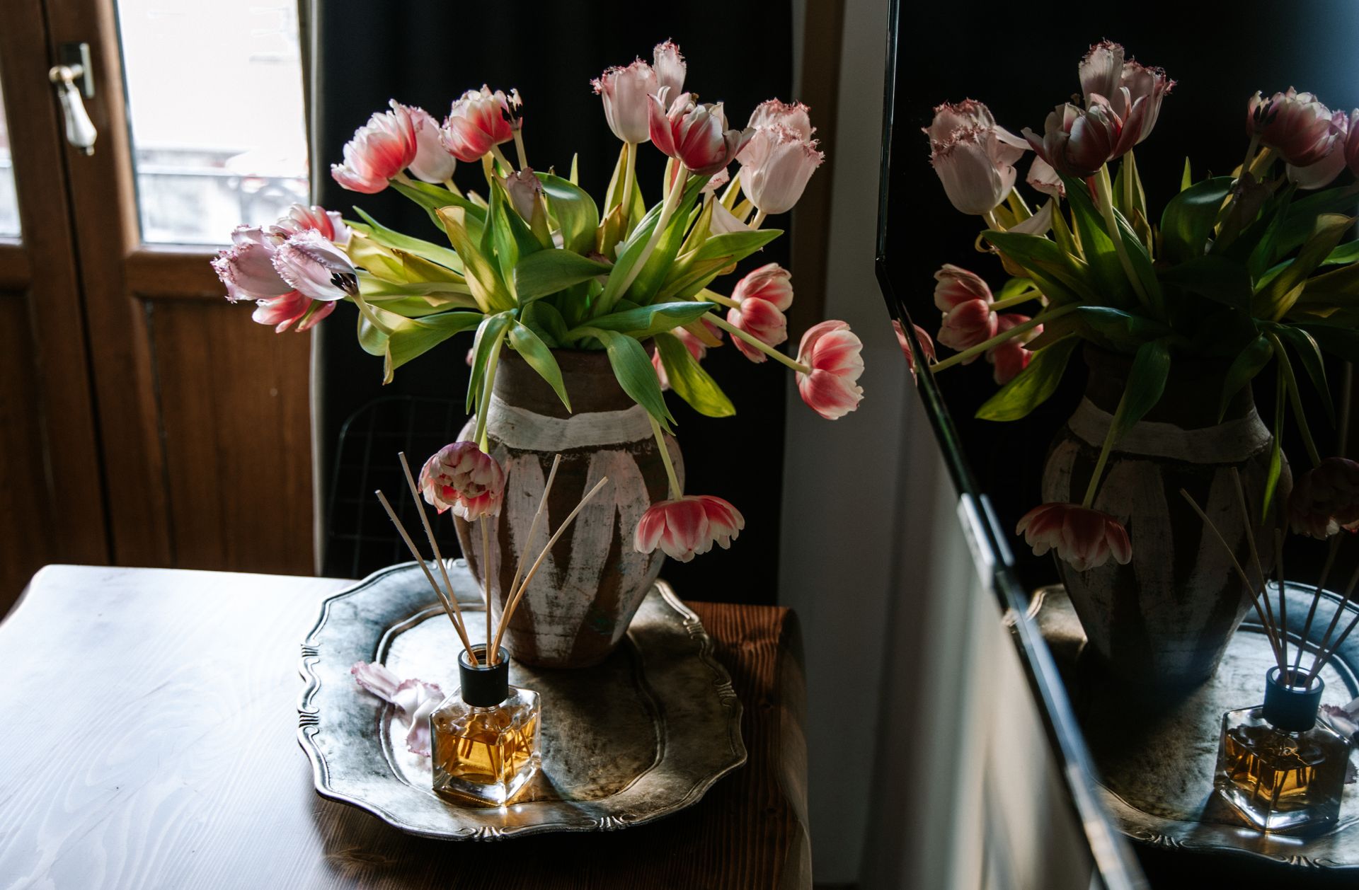 A decorative setup with a vase of tulips and aromatic diffuser on a tray indoors.